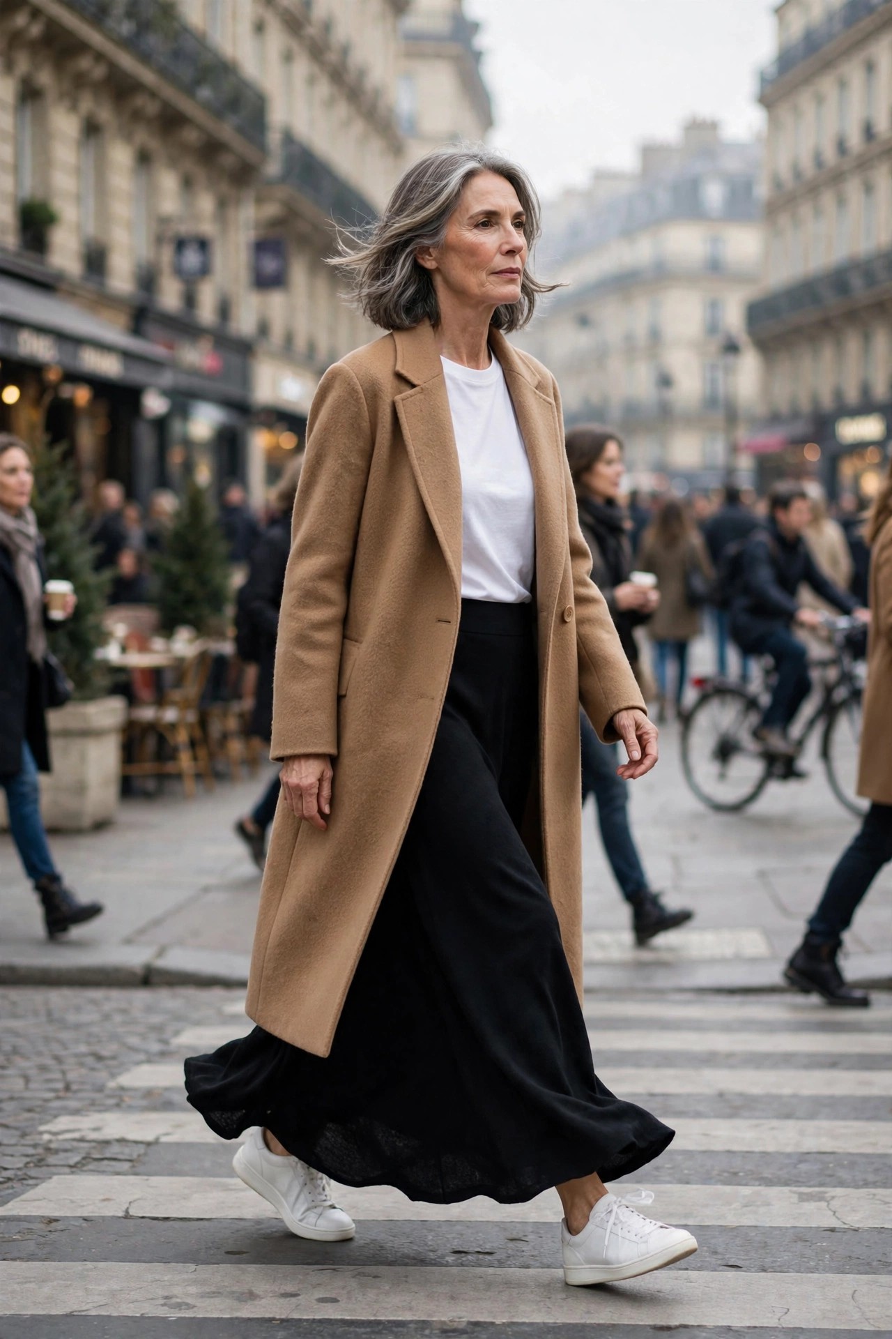 Woman over 50 in a black maxi skirt with a camel coat and white sneakers