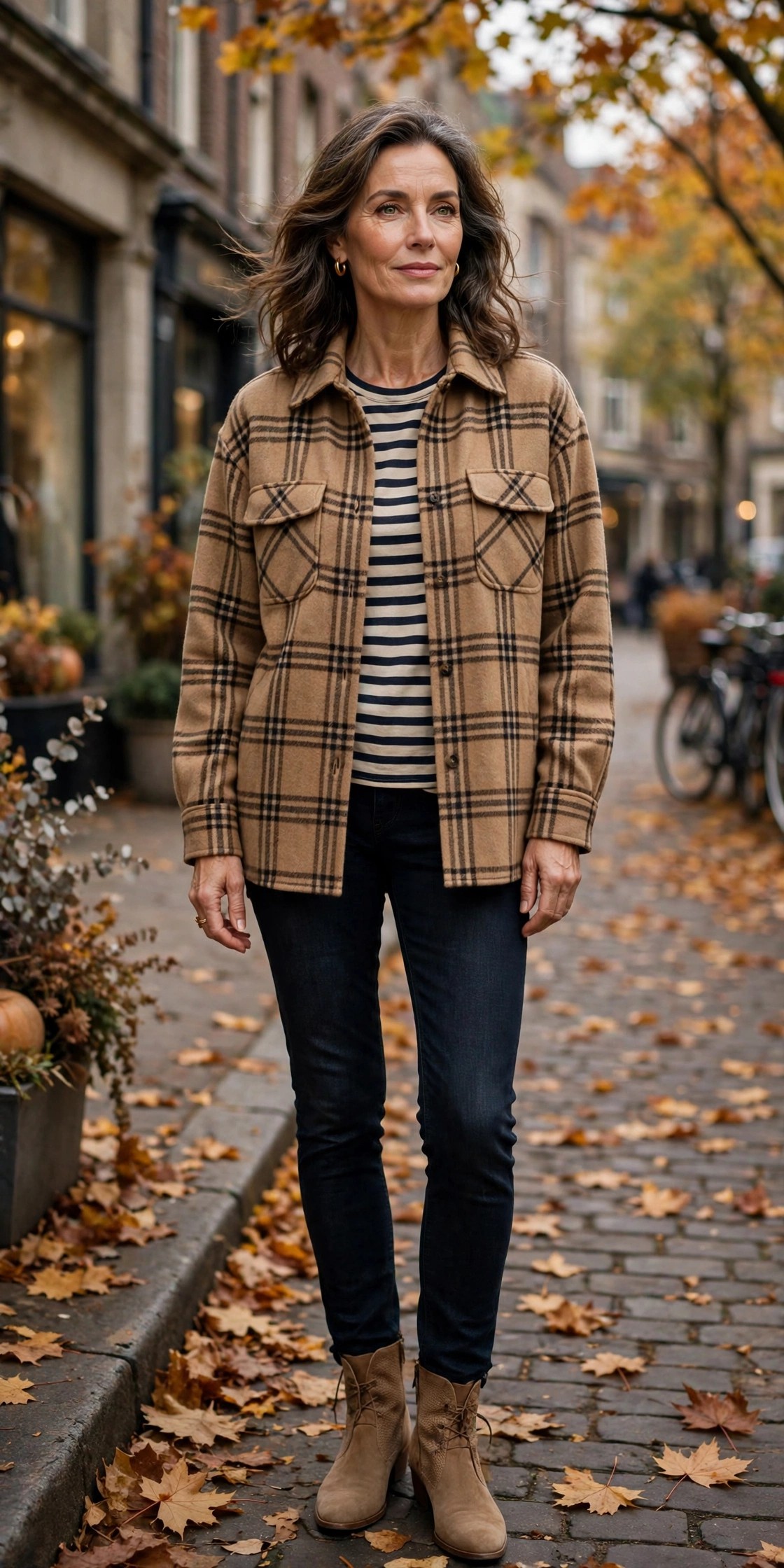 Woman in her 50s in a camel plaid shacket over a striped tee with dark jeans and tan ankle boots