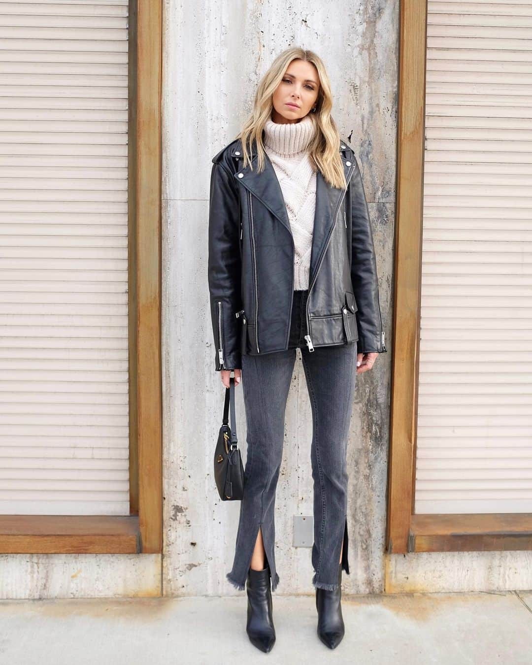 Woman wearing a black moto jacket with a cream knit sweater and dark jeans