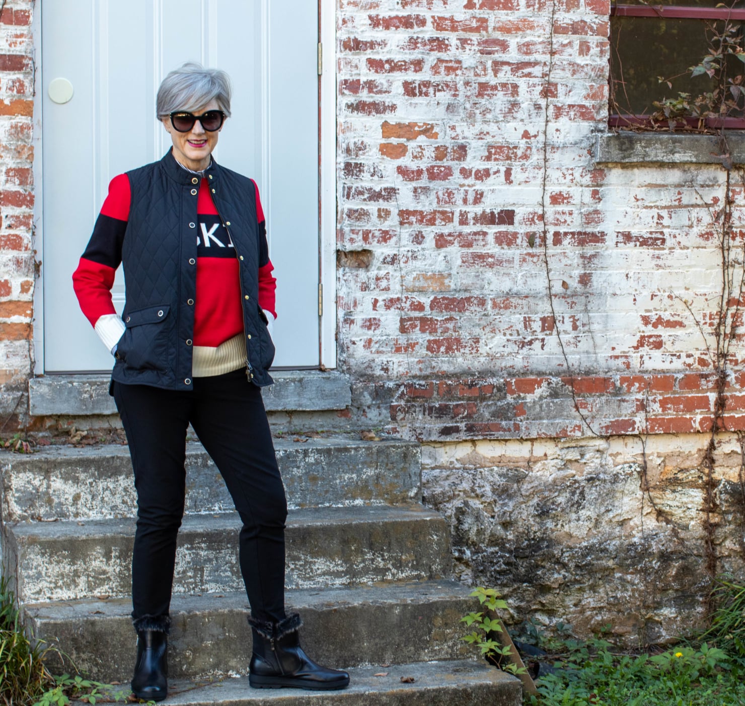 Black puffer vest over a red sweater with dark jeans and tall boots for cold fall days