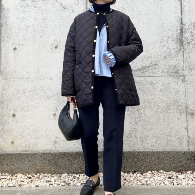 Woman over 50 in black quilted jacket, black turtleneck and tailored trousers