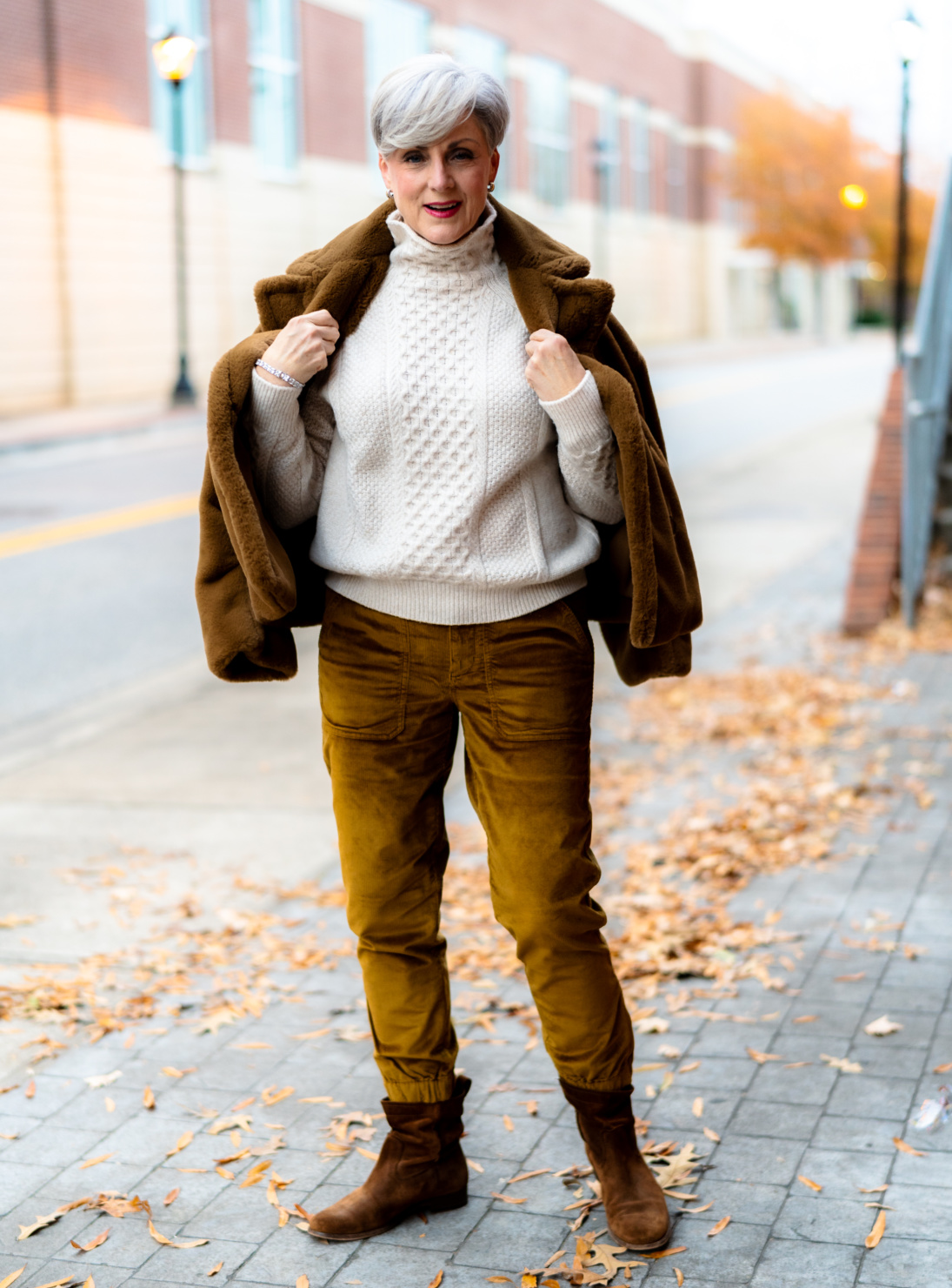 Woman over 50 in cream cable knit sweater with corduroy pants and brown boots