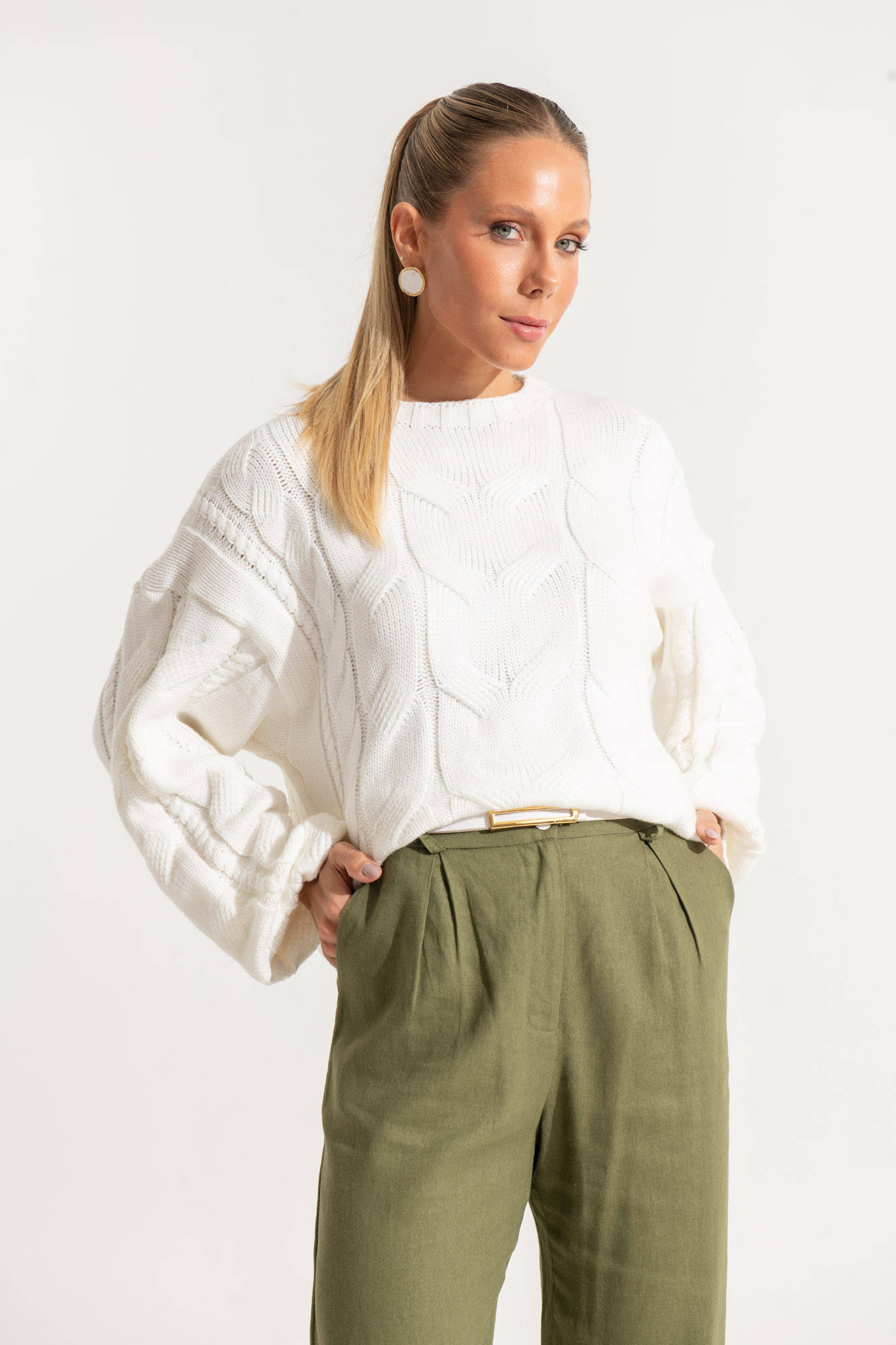 White cable knit sweater with green trousers and gold accessories