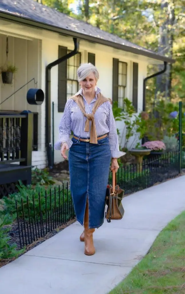 Woman over 50 wearing a striped shirt, long denim A-line skirt and tan Chelsea boots