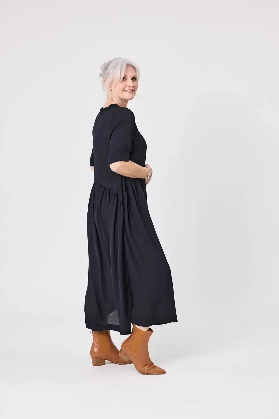 Woman over 50 wearing a black midi dress with tan leather Chelsea boots