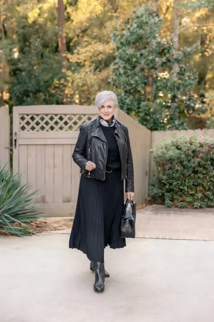 Woman over 50 wearing a black pleated midi skirt, leather jacket and black Chelsea boots