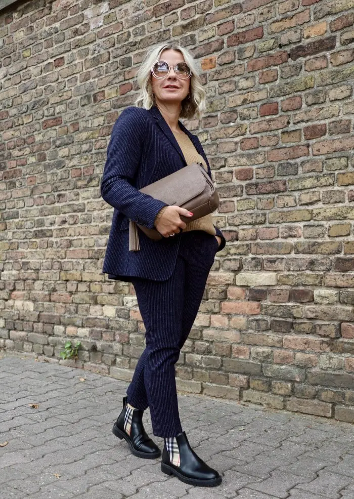 Woman over 50 wearing a navy pinstripe trouser suit with black Chelsea boots for work