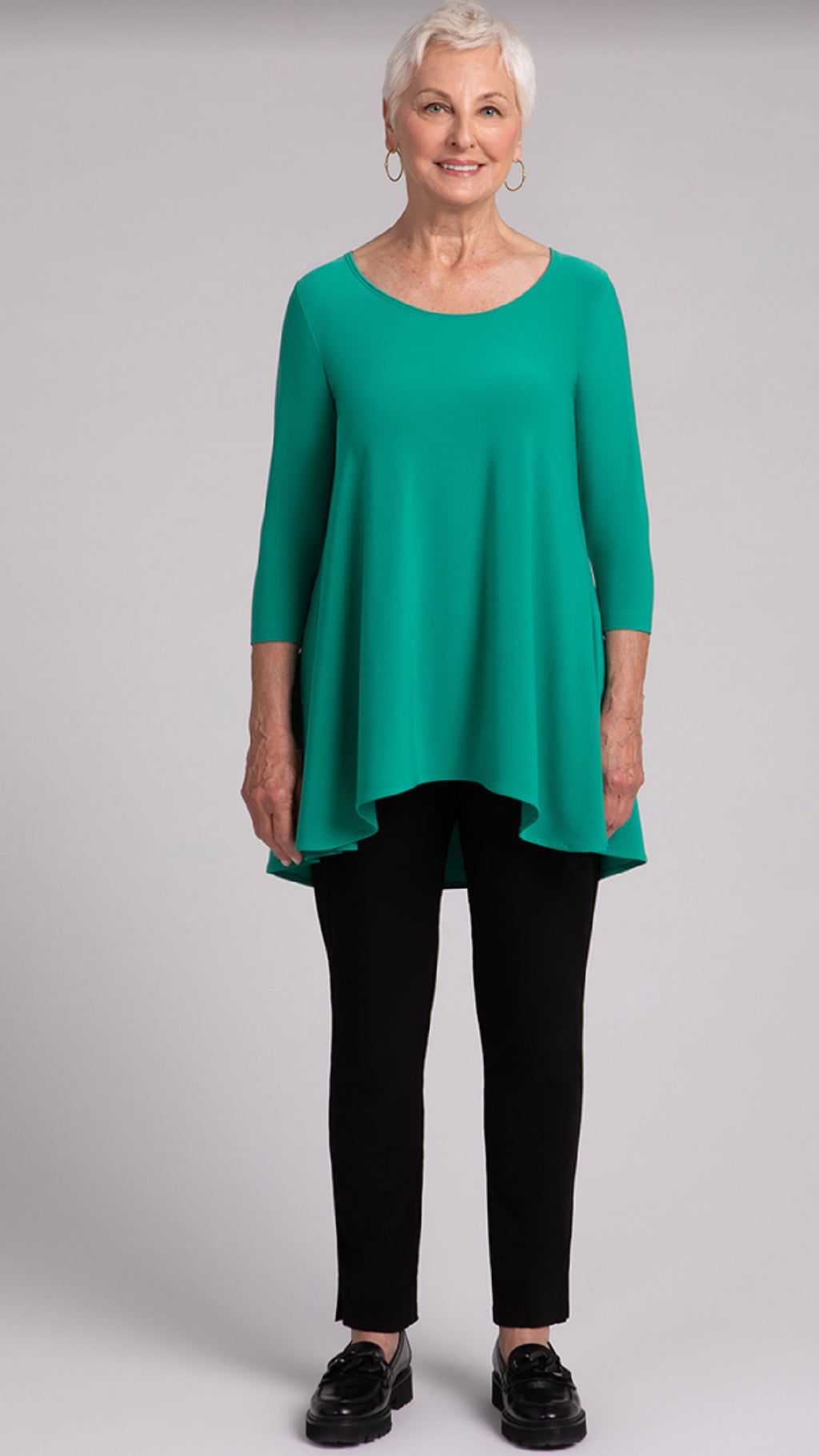 Plus size woman over 60 wearing emerald tunic with black ponte trousers and loafers