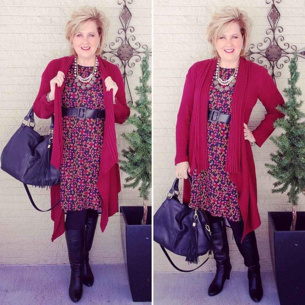 Woman over 50 in a burgundy long cardigan over a black knit dress with tall boots