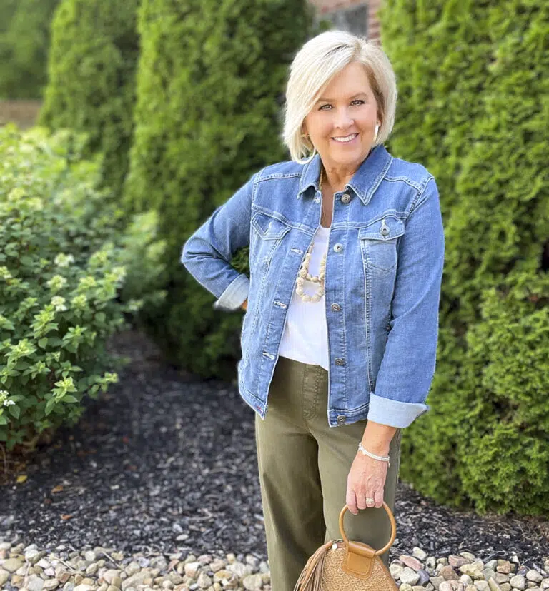 Woman over 50 wearing denim shacket over white tee with olive trousers