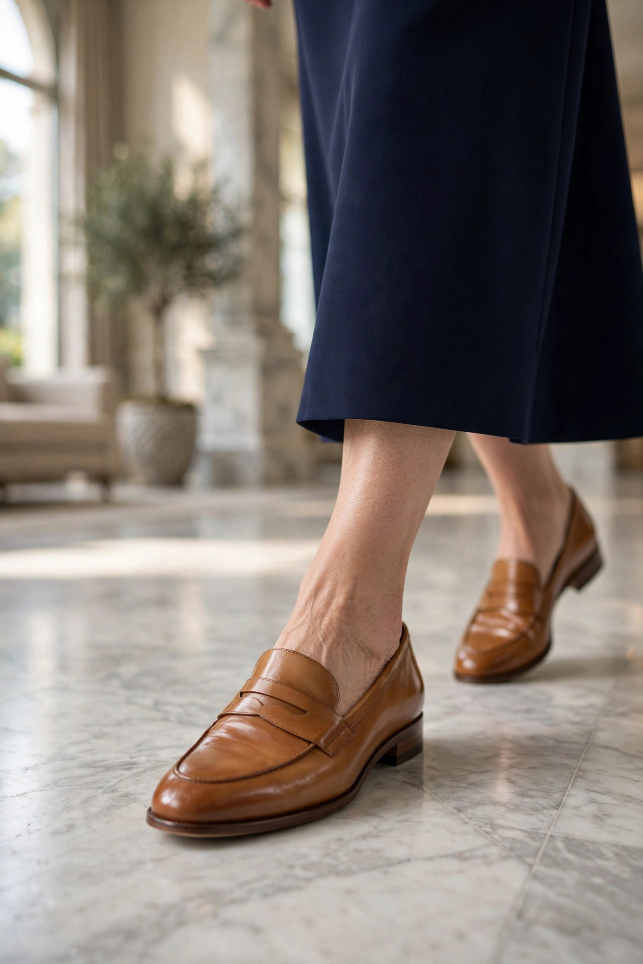 Polished tan leather loafers worn with a navy dress on a marble floor
