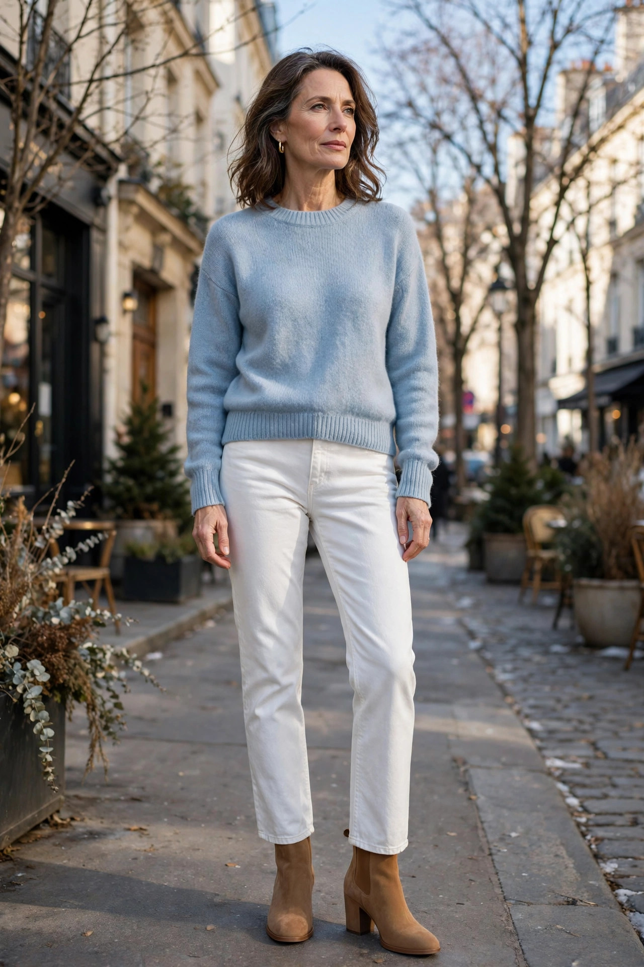 Woman over 50 in a powder blue sweater and white jeans on a sunny winter street
