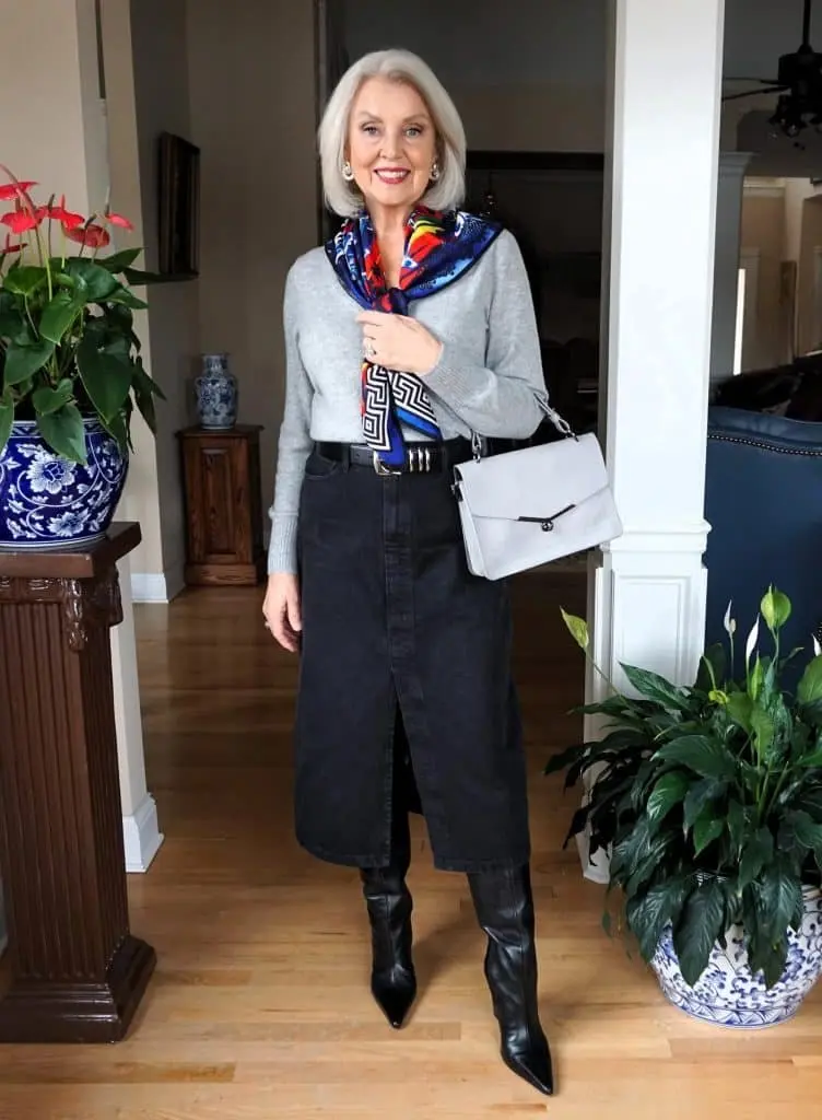 Woman over 60 wearing a black denim midi skirt with black knee-high boots and a colourful scarf