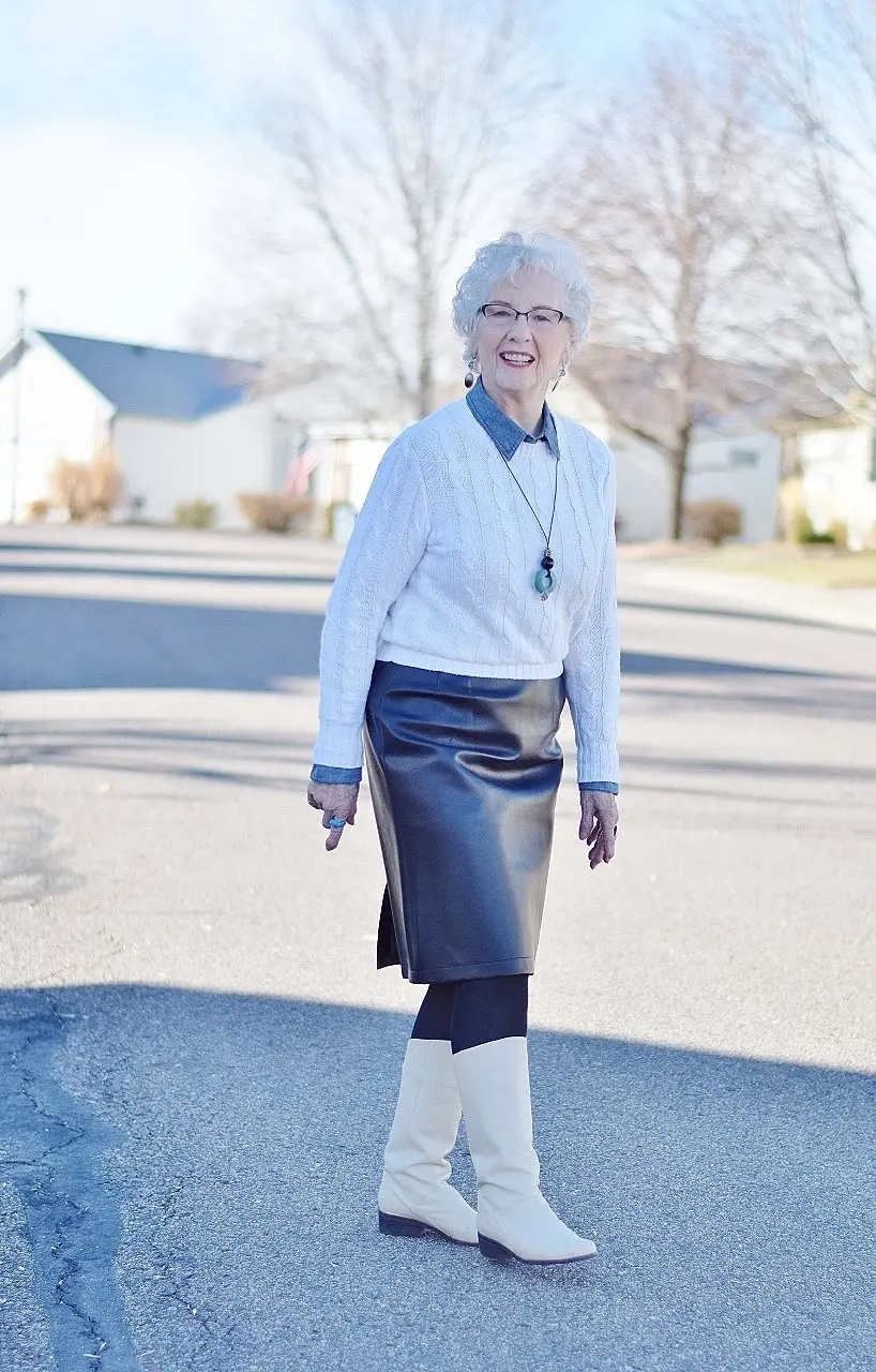 Woman over 60 wearing a black leather pencil skirt with white knee-high boots and a crisp white shirt
