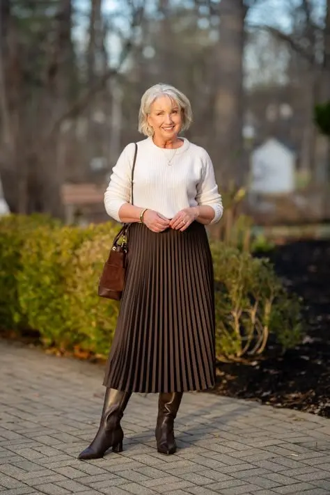 Woman over 50 wearing a pleated midi skirt with knee-high boots, graceful and polished