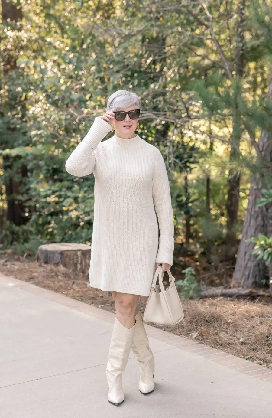Woman over 60 with silver hair in a cream sweater dress with white knee-high boots