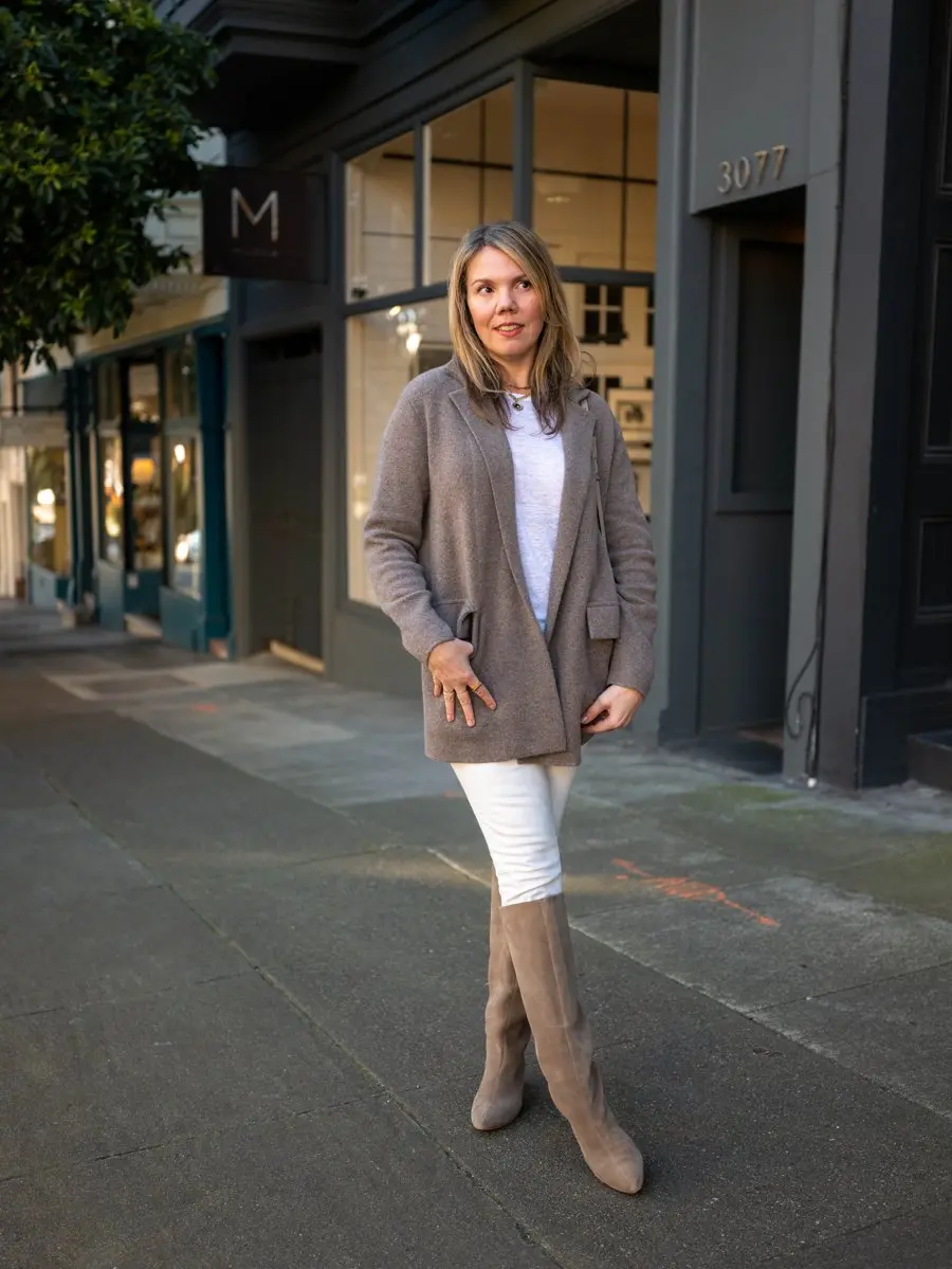 Woman over 50 wearing white jeans with taupe suede knee-high boots and a soft cardigan in winter