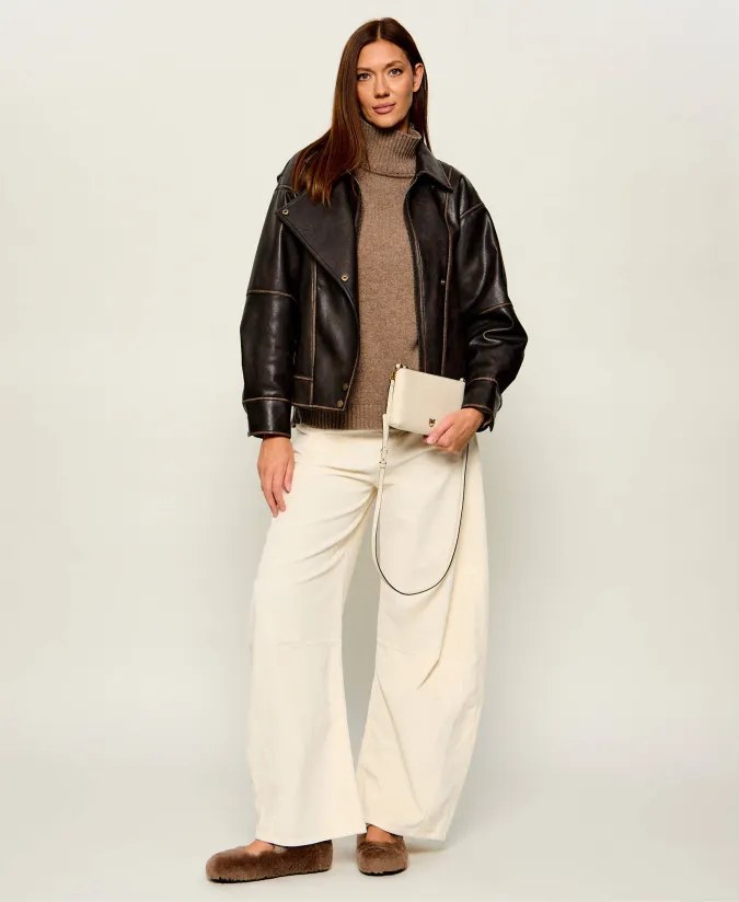 Woman wearing a black leather jacket with a knit sweater and cream wide trousers