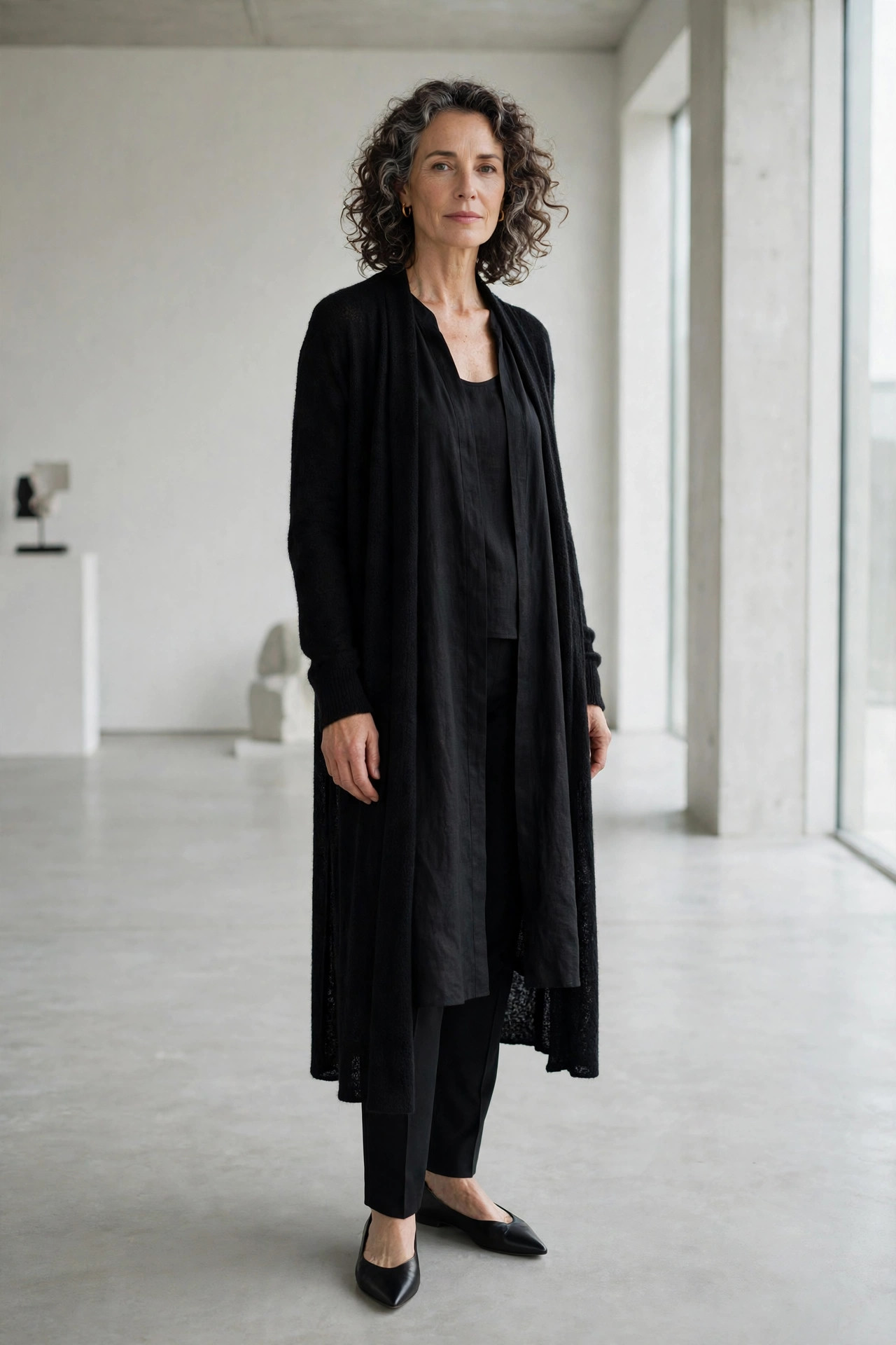 Woman over 50 wearing a black tunic dress over slim black trousers with a long cardigan