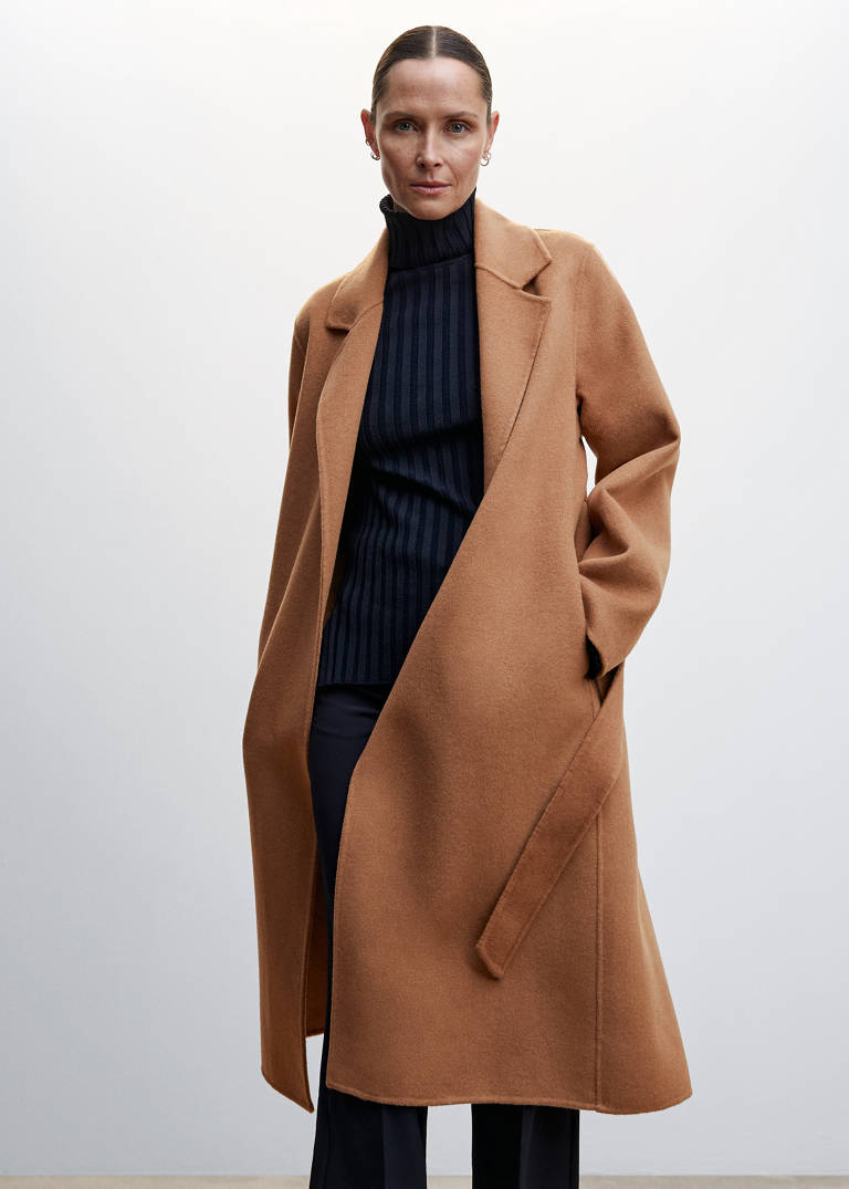Long camel vest over a black turtleneck and black trousers — slimming fall outfit