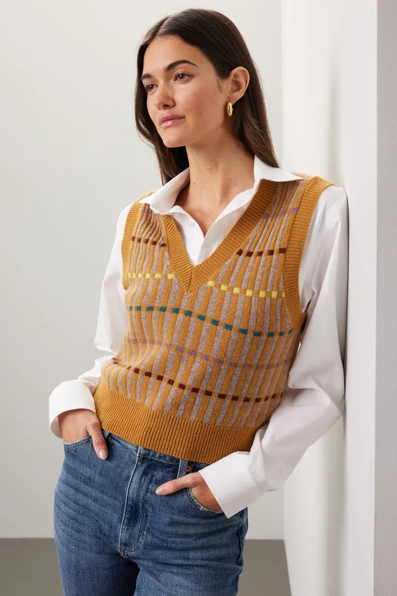 Mustard knit vest over a white shirt with navy trousers on a woman over 50
