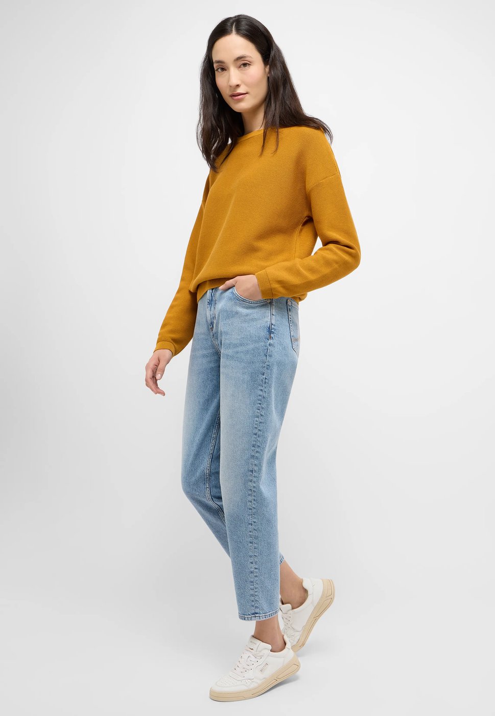 Mustard yellow sweater with light wash jeans and white sneakers on a woman over 50