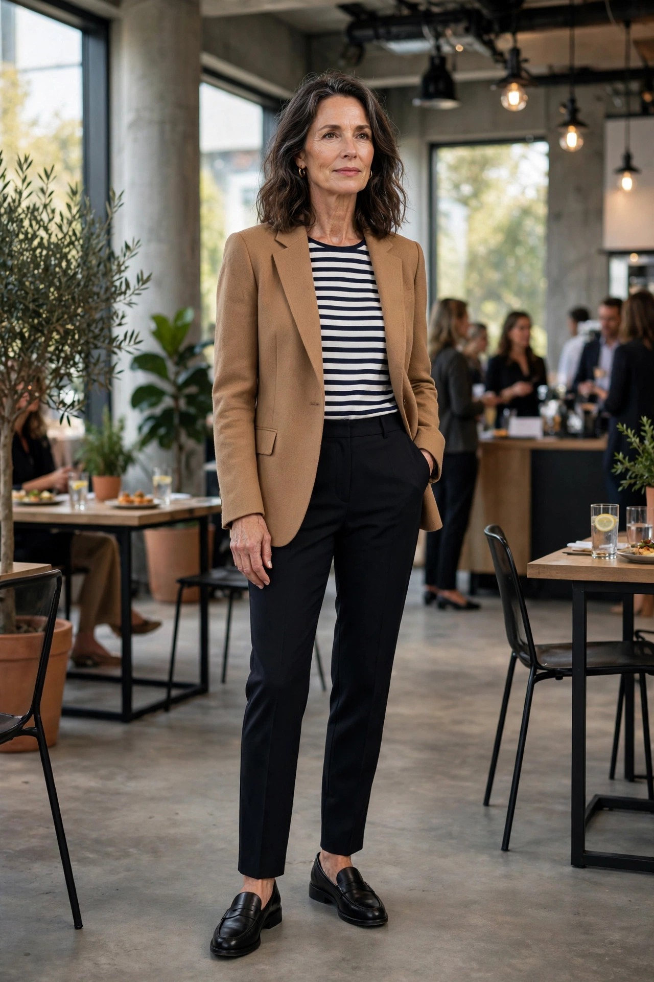 Woman over 50 in a camel blazer, striped top and black trousers at an industry mixer