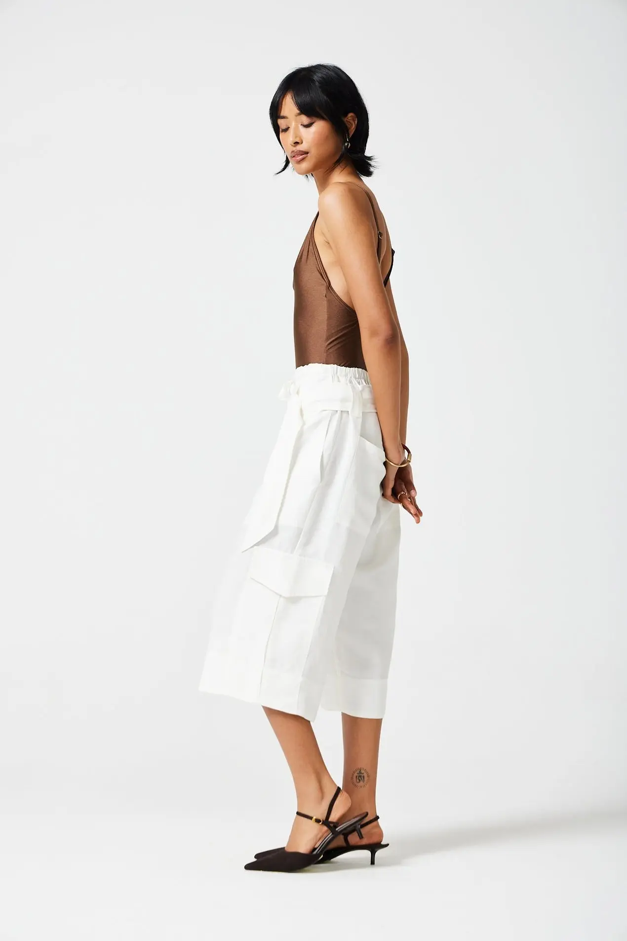 Woman wearing a chocolate brown deep-cut bodysuit with white wide-leg culottes and black mules