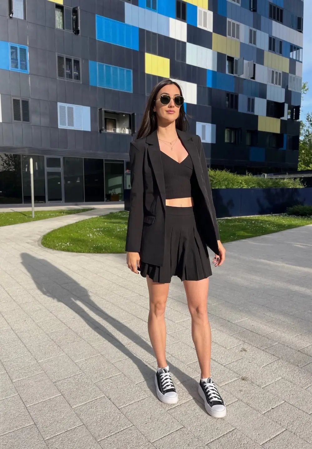 Woman wearing a black oversized blazer over a black pleated mini skirt with sneakers