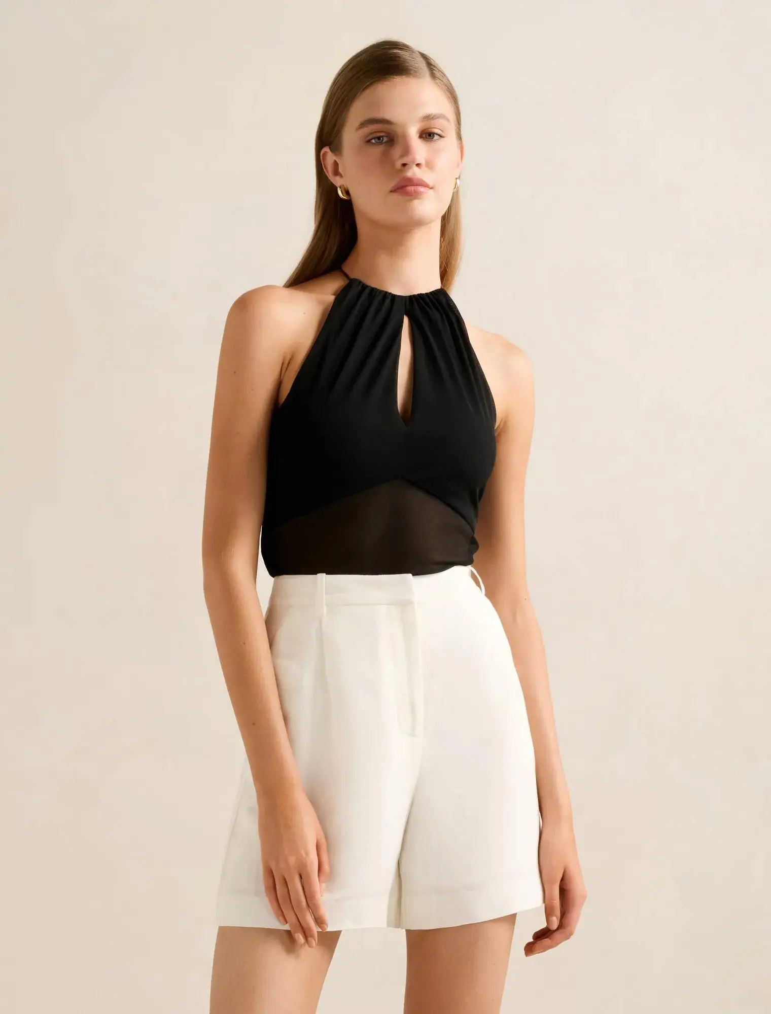 Woman wearing a black halter top with a sheer mesh panel and white tailored shorts