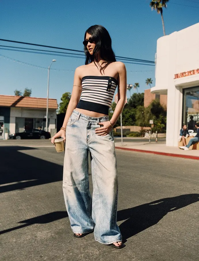 Woman wearing a black and white striped tube top with light-wash baggy wide-leg jeans on a city street