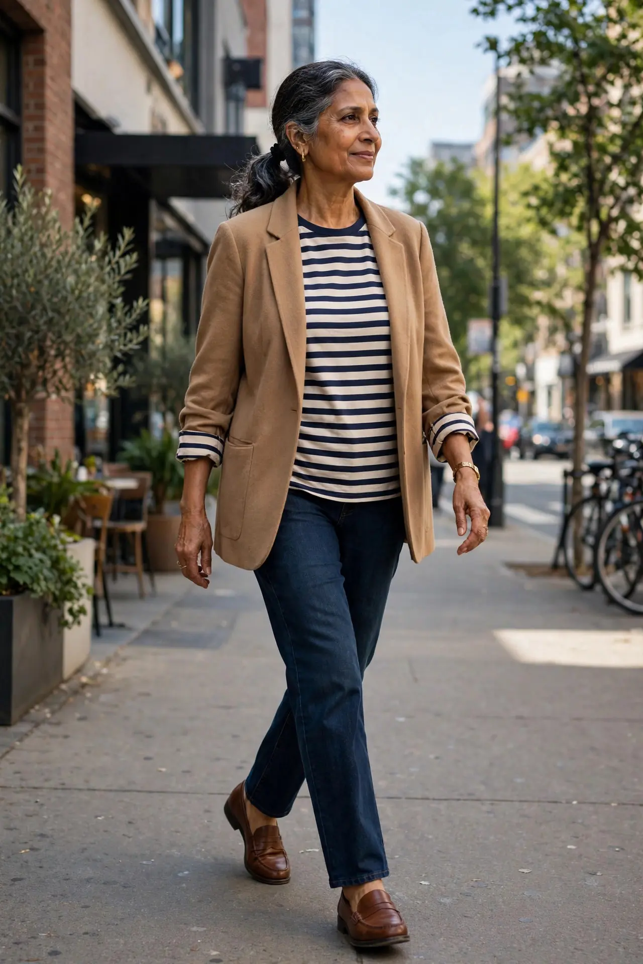 Woman over 60 wearing dark straight-leg jeans, a striped Breton tee and a camel blazer with brown loafers