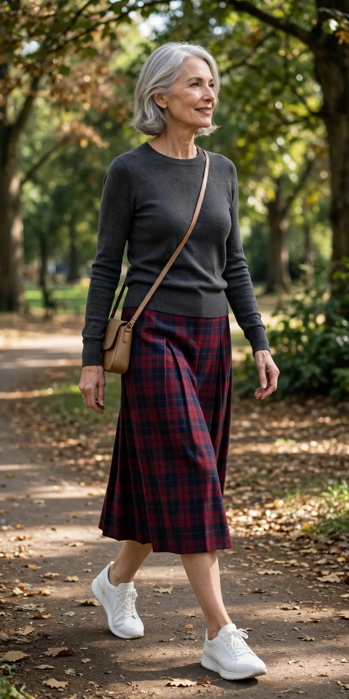 Woman over 60 wearing white leather sneakers with a plaid midi skirt and charcoal knit in a park