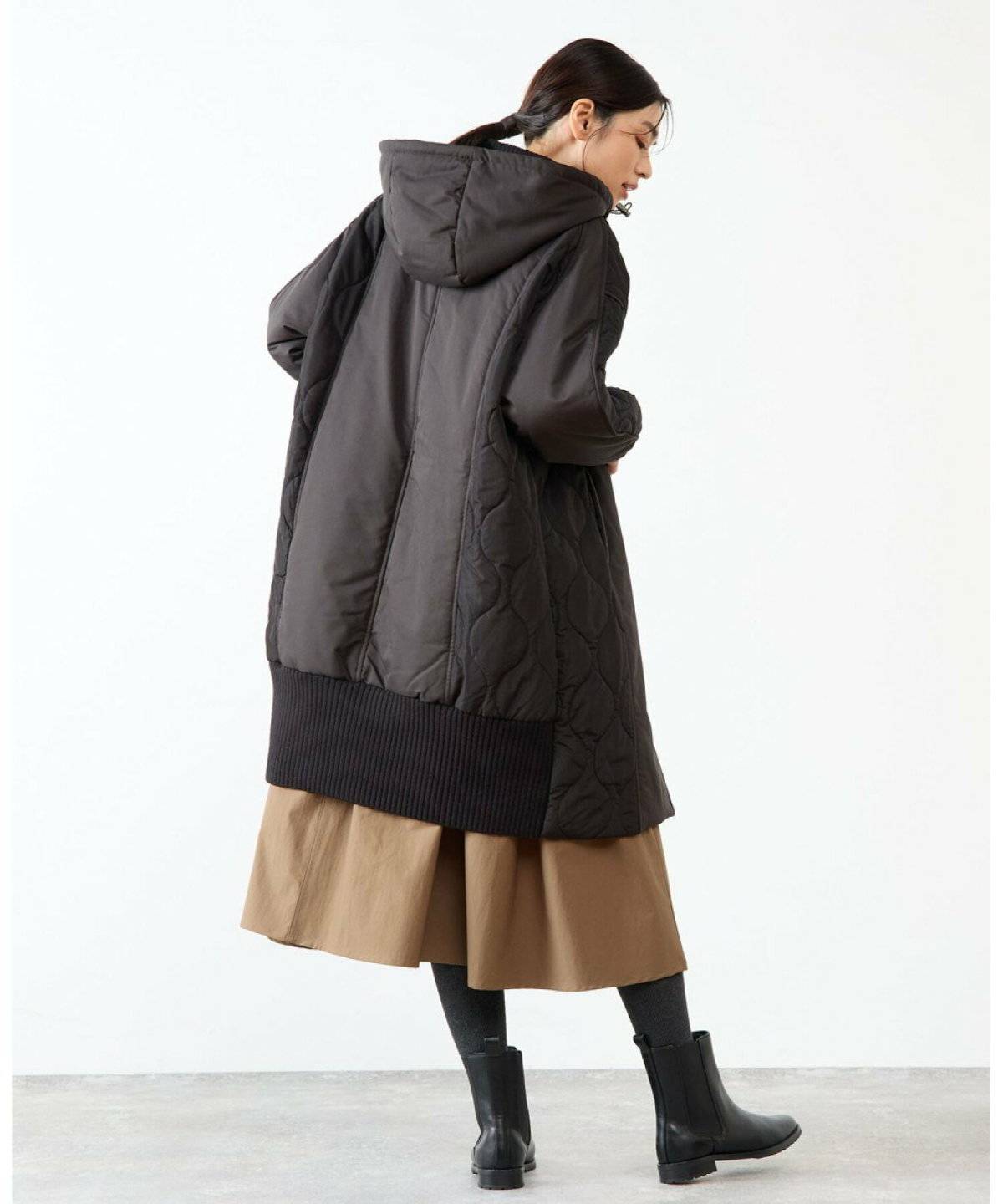 Woman over 50 wearing quilted jacket over rust knit dress with ankle boots