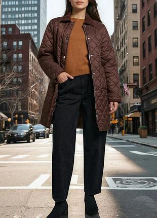 Woman over 50 layering a quilted jacket under a long camel wool coat