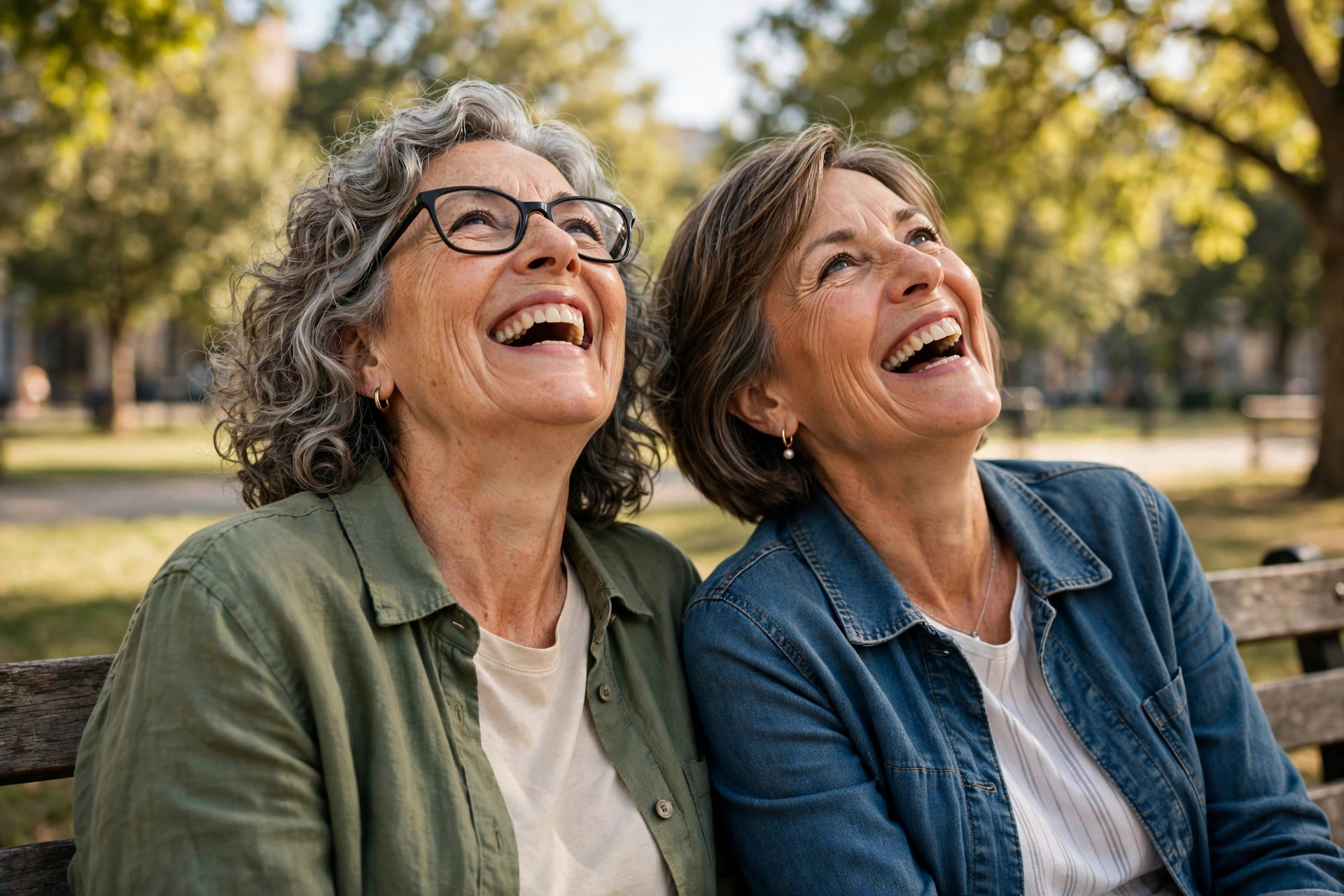 Two women in their 60s laughing together on a park bench