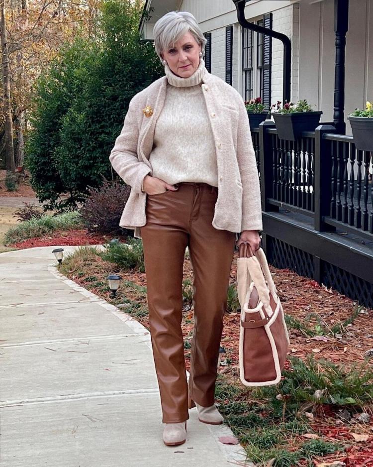 Woman over 60 wearing suede shacket with cream knit and trousers