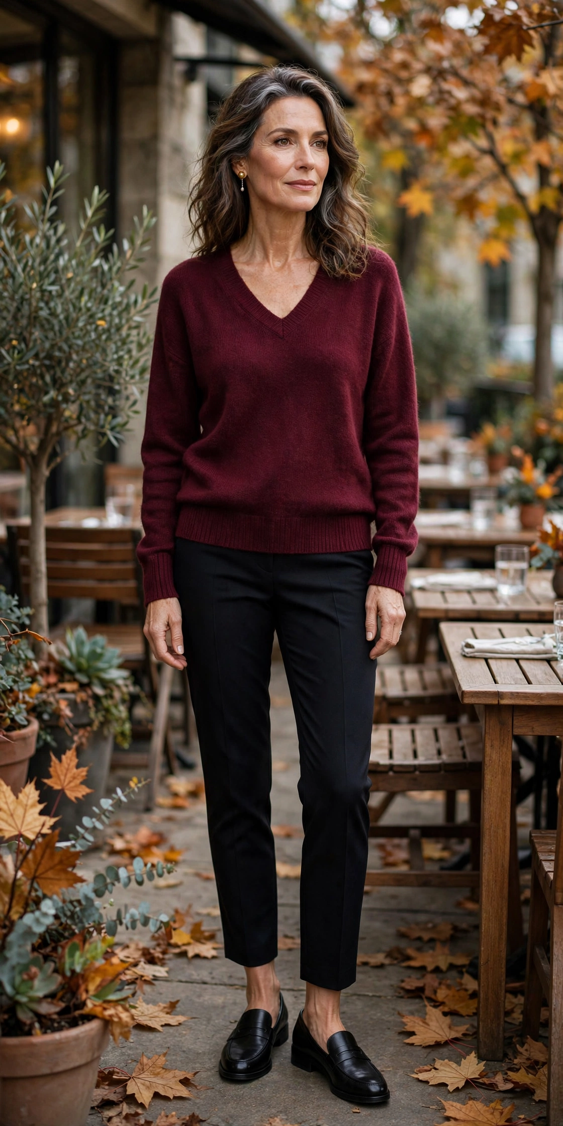Woman over 50 in a burgundy v-neck sweater with black ankle trousers and loafers